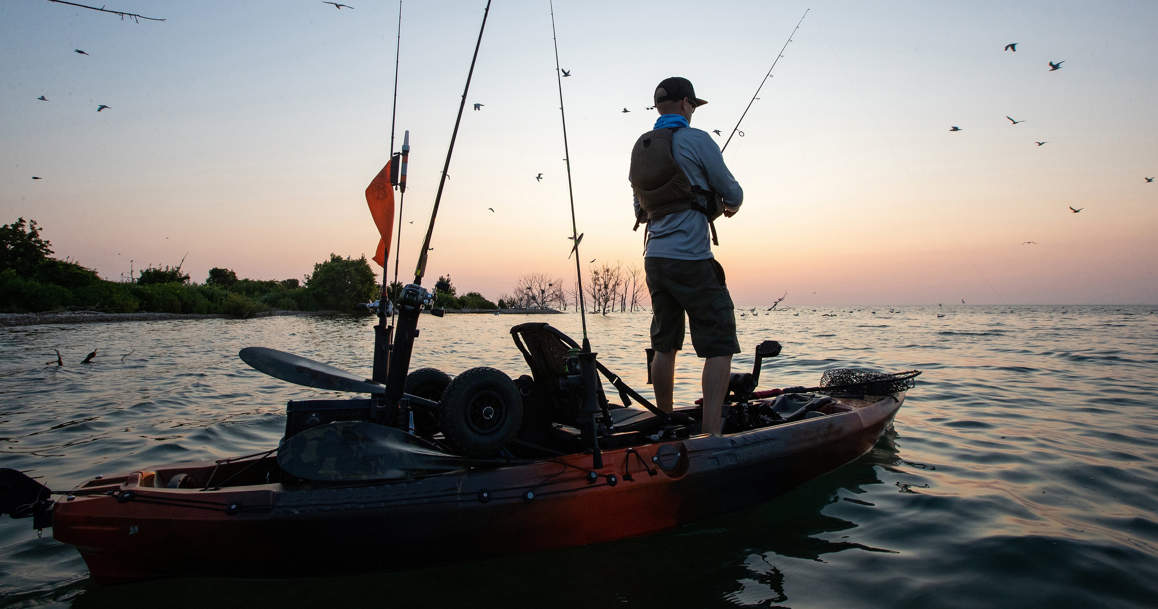 Seorang petualang berdiri di atas kayak memancing saat matahari terbenam di danau